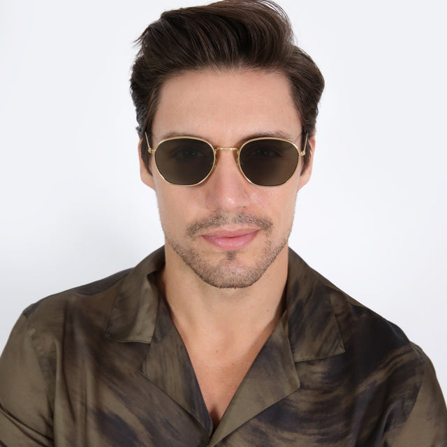 Model with short, brown hair combed sideways wearing Prince Sunglasses Gold with Olive Flat