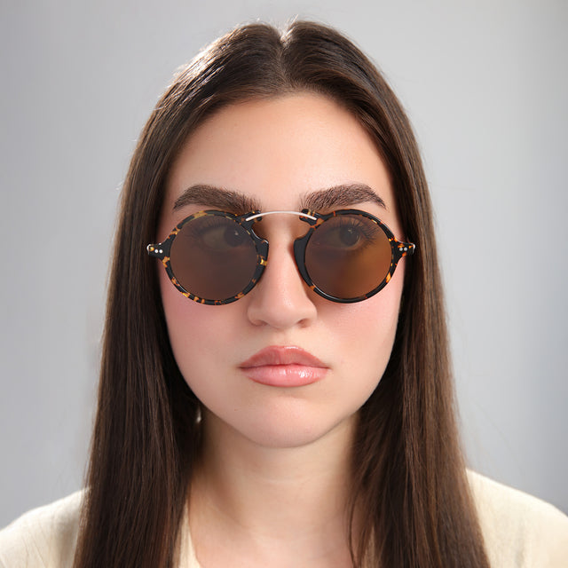 Brunette model in front of a grey wall wearing Roma II Sunglasses Flame/Gold with Brown Flat