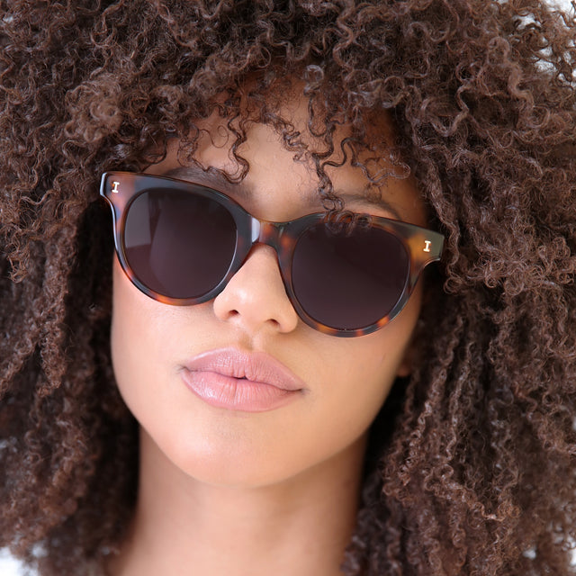 Brunette model with natural small curls wearing Sicilia Sunglasses Havana with Grey