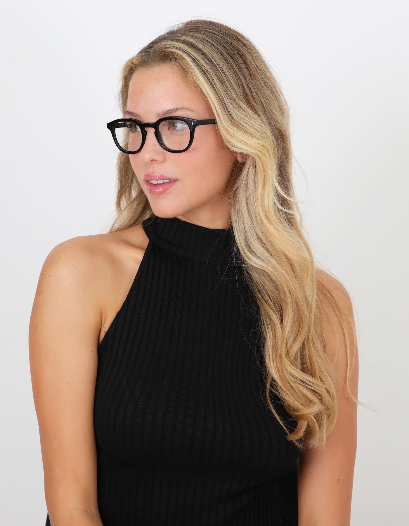 Blonde model with wavy hair in a high neck blouse wearing Slope Optical in Black.