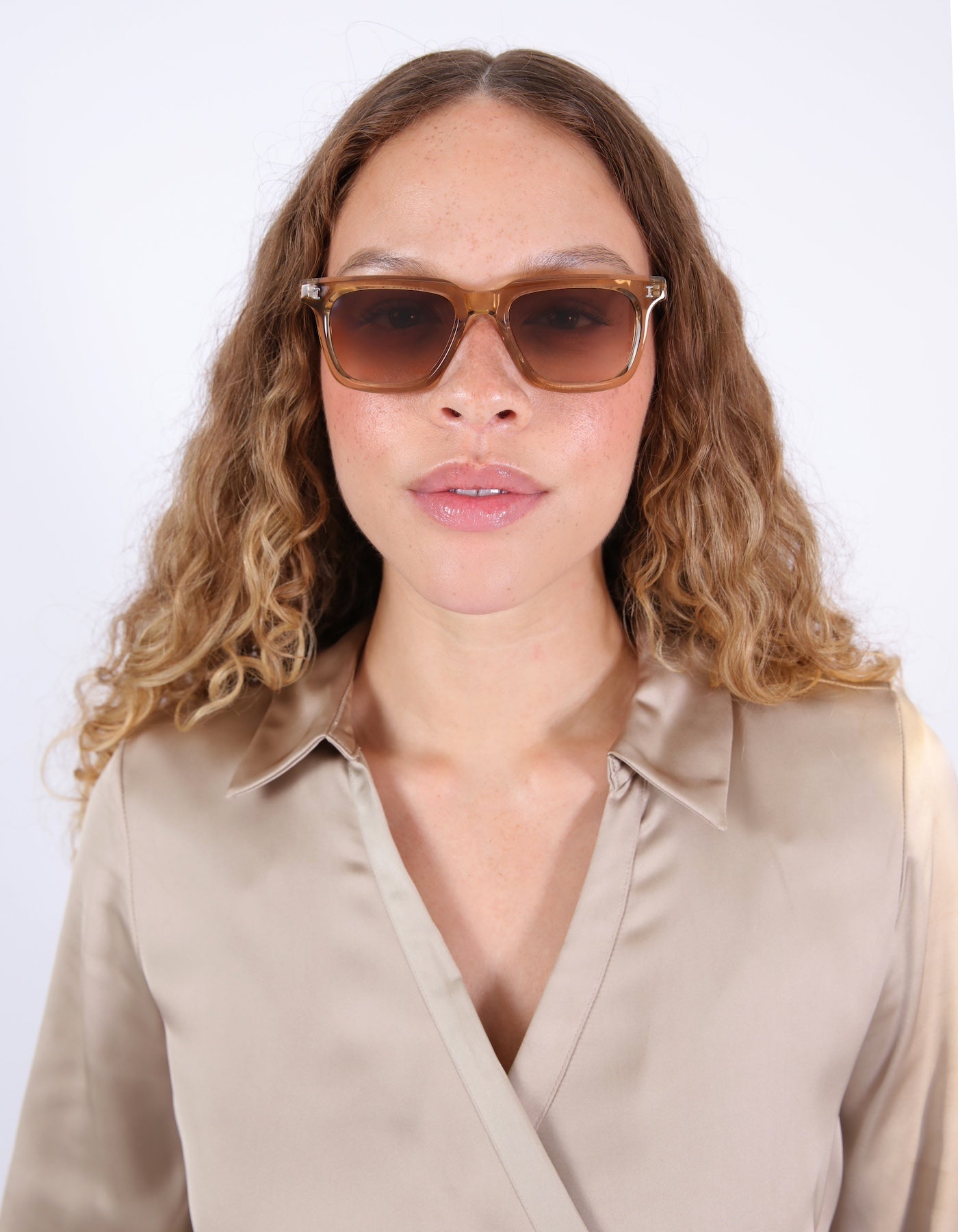 Brunette model with ombré, wavy hair in a silk blouse wearing Toscana Sunglasses in Brown.