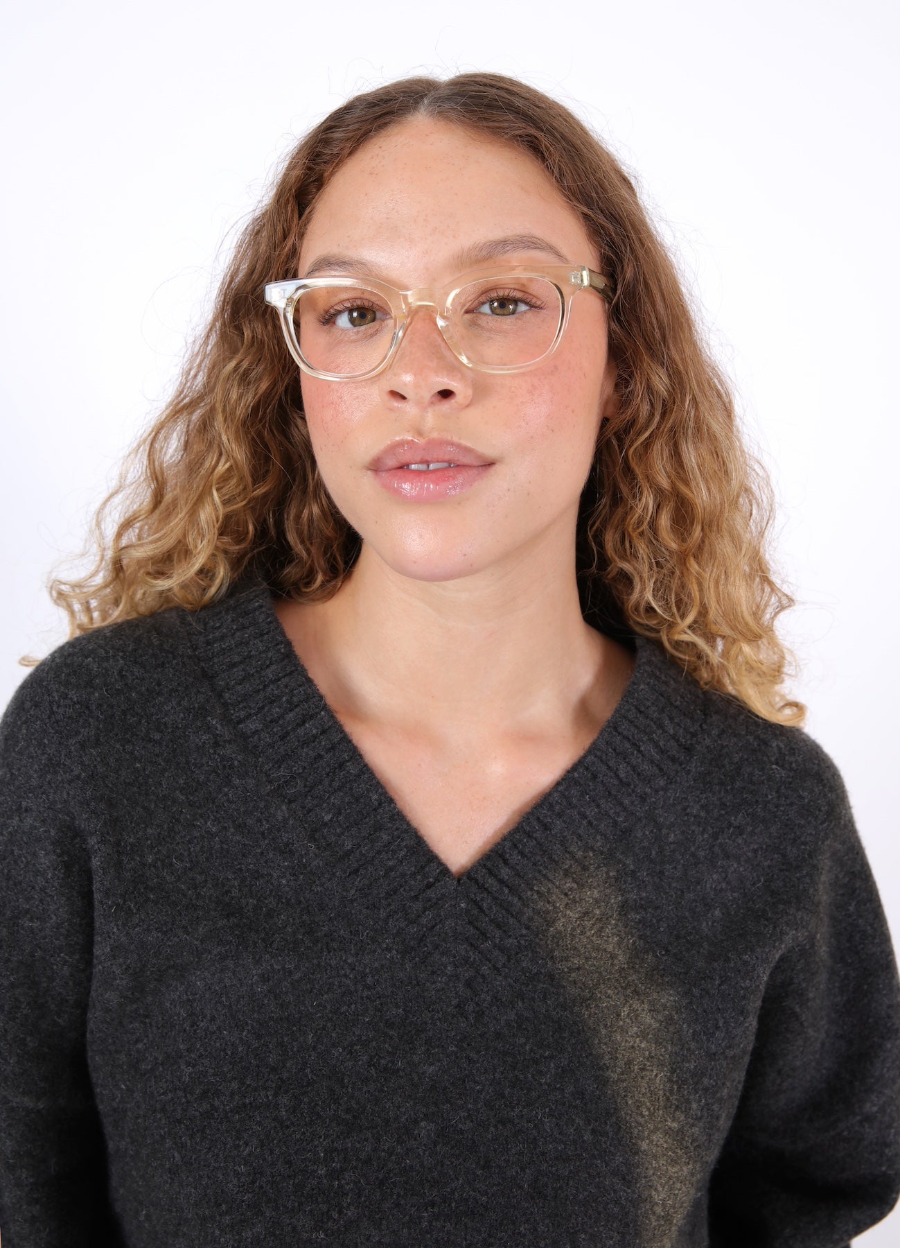 Brunette model with ombré wavy hair in a V-neck sweater wearing Veneto Optical in Champagne