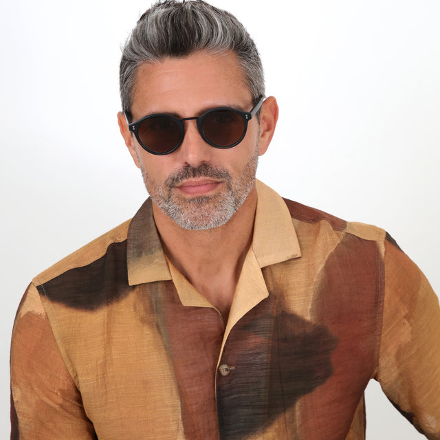 Model with salt and pepper hair and beard wearing Village Sunglasses Matte Black with Brown
