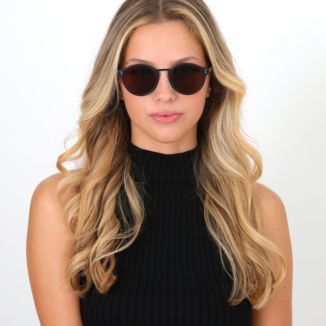 Blonde model with loose curls wearing Village Sunglasses Matte Black with Brown