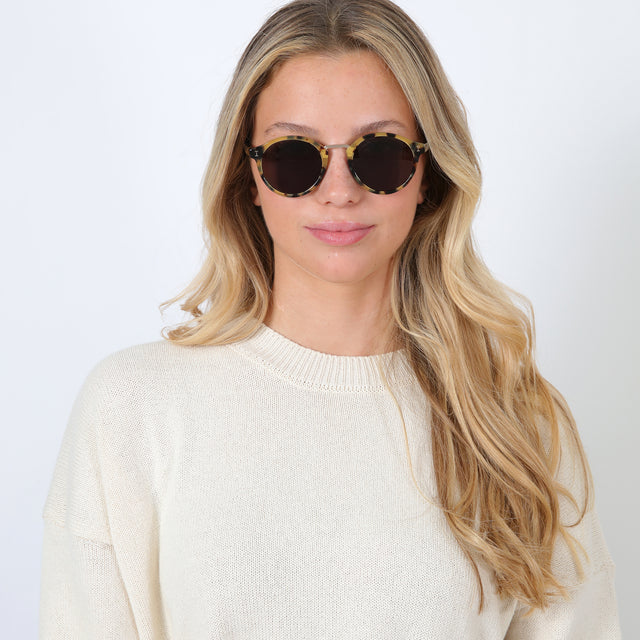 Blonde model with beach waves wearing Village Sunglasses Tortoise/Gold with Grey