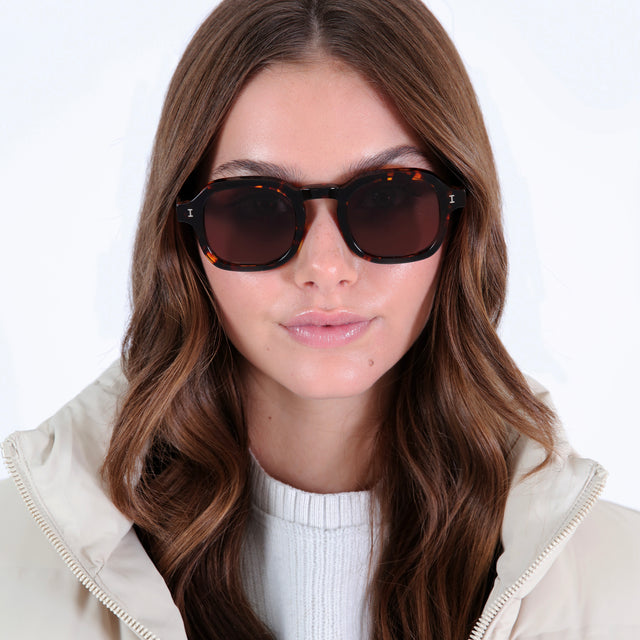 Brunette model with curled hair in a white puffer coat wearing Washington Sunglasses Star Tortoise with Brown Flat