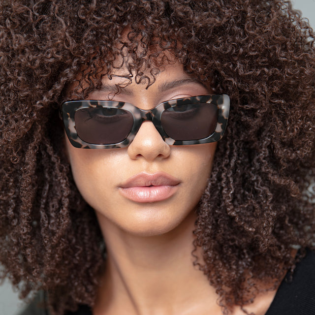 Brunette model with natural tight curls wearing Wilson Sunglasses White Tortoise with Grey Flat