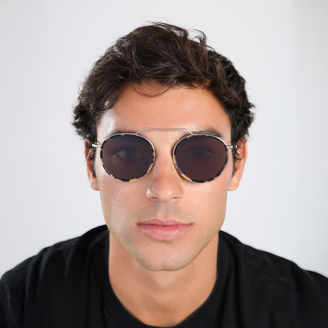 Another angle of the man with short brown hair in a black tee wearing Wynwood Ace Sunglasses Tortoise/Silver with Grey Flat