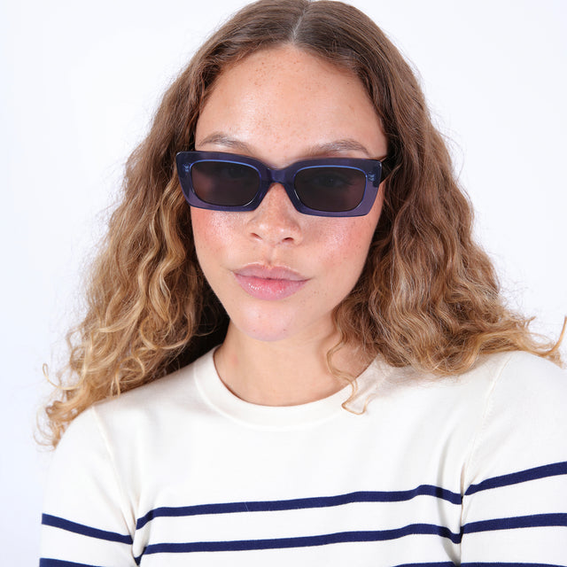 Brunette model with wavy ombre wearing nk x illesteva Wilson Sunglasses Cobalt/Black with Grey Flat