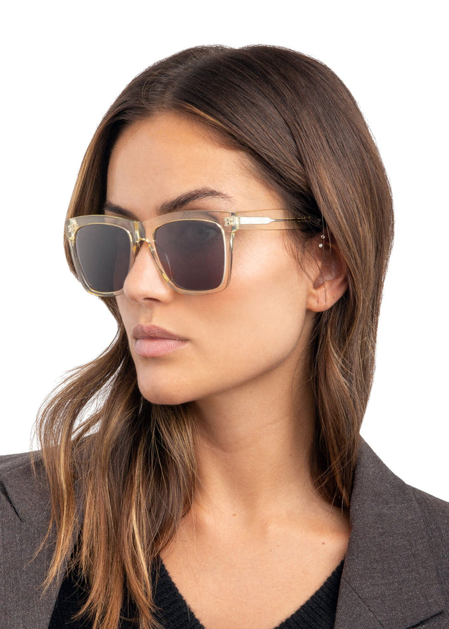 Angled pose of brunette model with wavy hair wearing Los Feliz Sunglasses Champagne with Grey