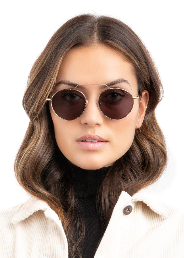Brunette model with wavy hair wearing Wynwood II Sunglasses Rose Gold with Grey Flat Lenses