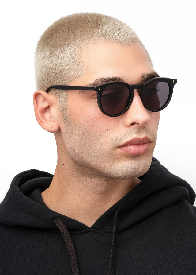 Angled pose of model with blonde buzzcut wearing Sterling Sunglasses Matte Black with Grey Flat