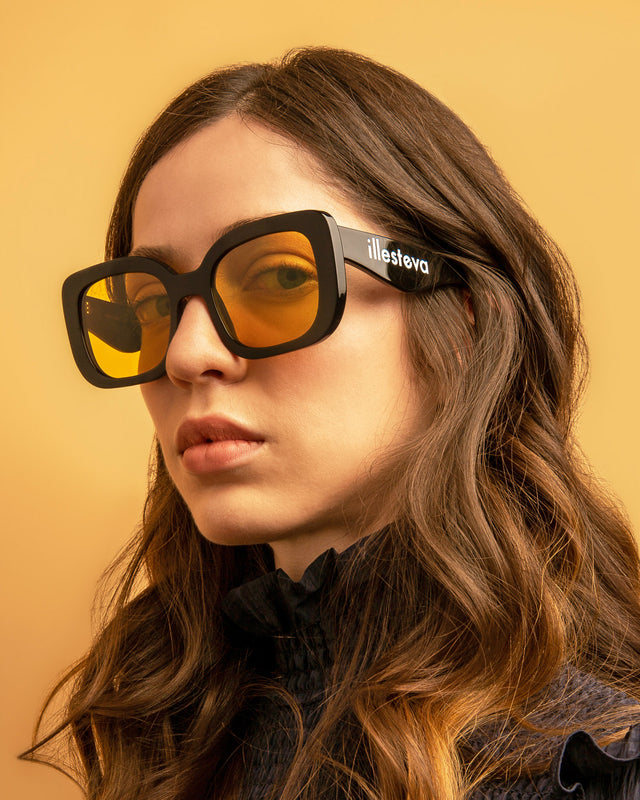 Brunette model with wavy hair wearing Anastasia Sunglasses Black with Honey See Through