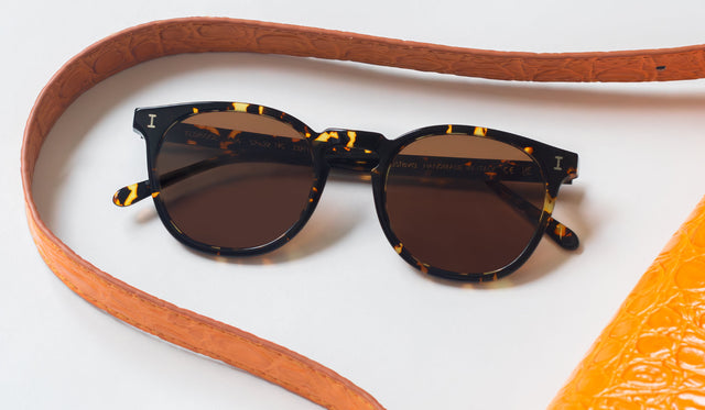 Eldridge Sunglasses in Flame near a brown leather purse