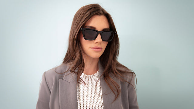 Brunette model in a gray blazer wearing Portugal Sunglasses in Black with Grey Flat