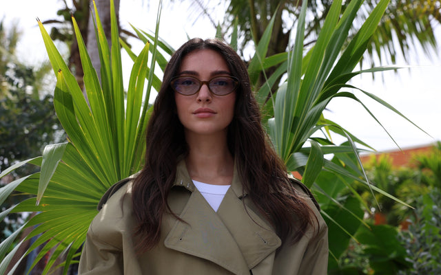 Woman in a trench coat wearing the Sheila Sunglasses in Moss with Light Blue See Through lenses