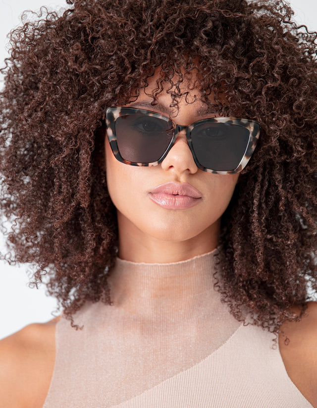 Brunette model with natural, tight curls wearing Barcelona Sunglasses in White Tortoise with Grey Flat