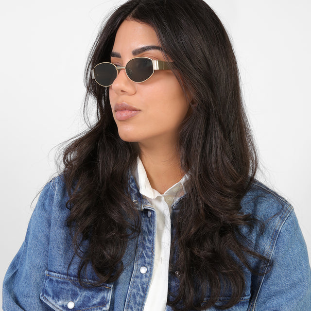 Brunette model in a denim jacket looking right wearing Bellagio Sunglasses Brushed Gold with Grey