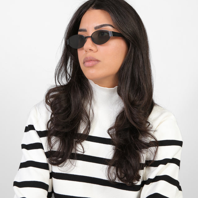 Brunette model in a black and white striped turtleneck wearing Bellagio Sunglasses Matte Black with Grey