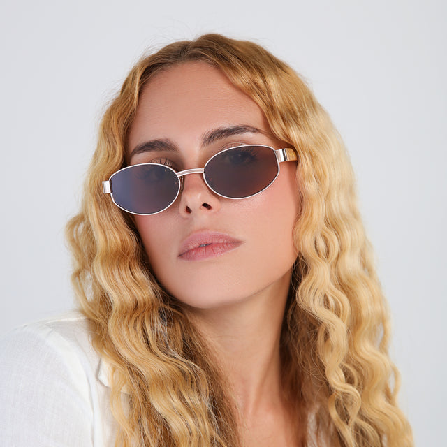 Blond woman with wavy hair in a white blouse wearing Bellagio A Sunglasses Rose Gold/Honey Gold with Brown