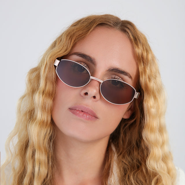 Another angle of blond woman with wavy hair in a white blouse wearing Bellagio A Sunglasses Rose Gold/Honey Gold with Brown