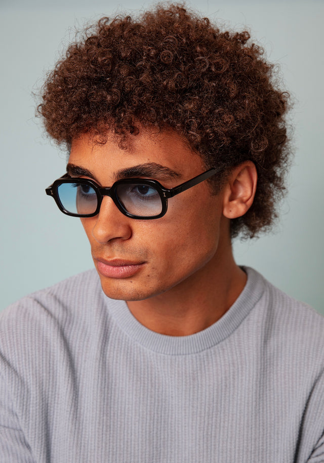 Model with short, tight curls wearing Berlin Sunglasses in Black with Blue Gradient See Through