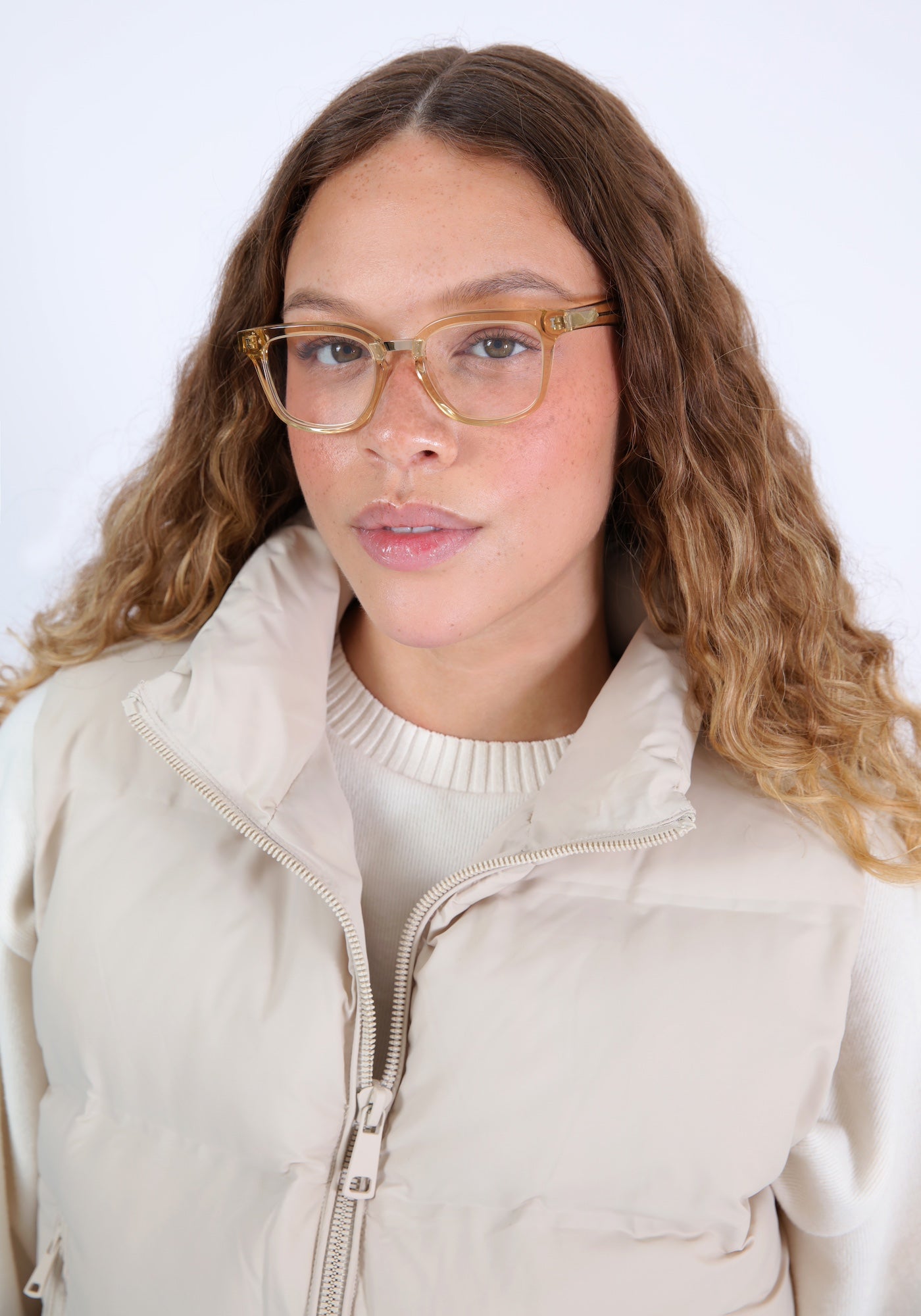 Brunette model with ombré, curled hair in a cream puffer vest wearing Bobby Optical in Citrine