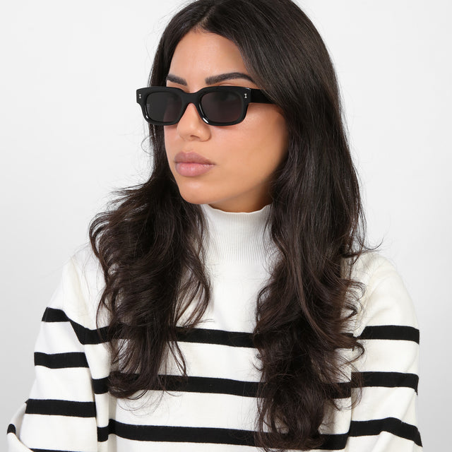 Brunette model in a black and white turtleneck looking right wearing Cali E Sunglasses Black with Grey