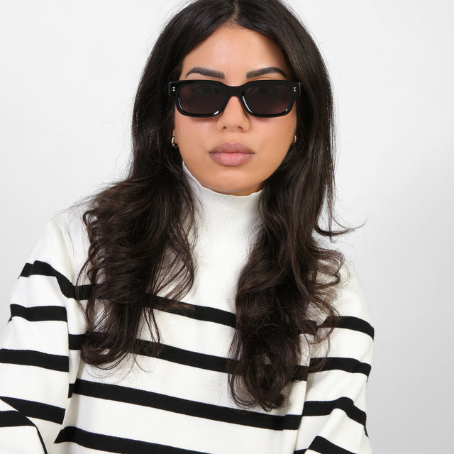 Brunette model in a black and white turtleneck wearing Cali E Sunglasses Black with Grey