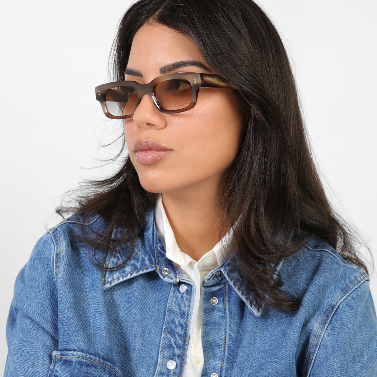 Woman wearing Cali E Sunglasses in Java with Taupe Gradient lenses, Brunette model in a denim jacket looking right