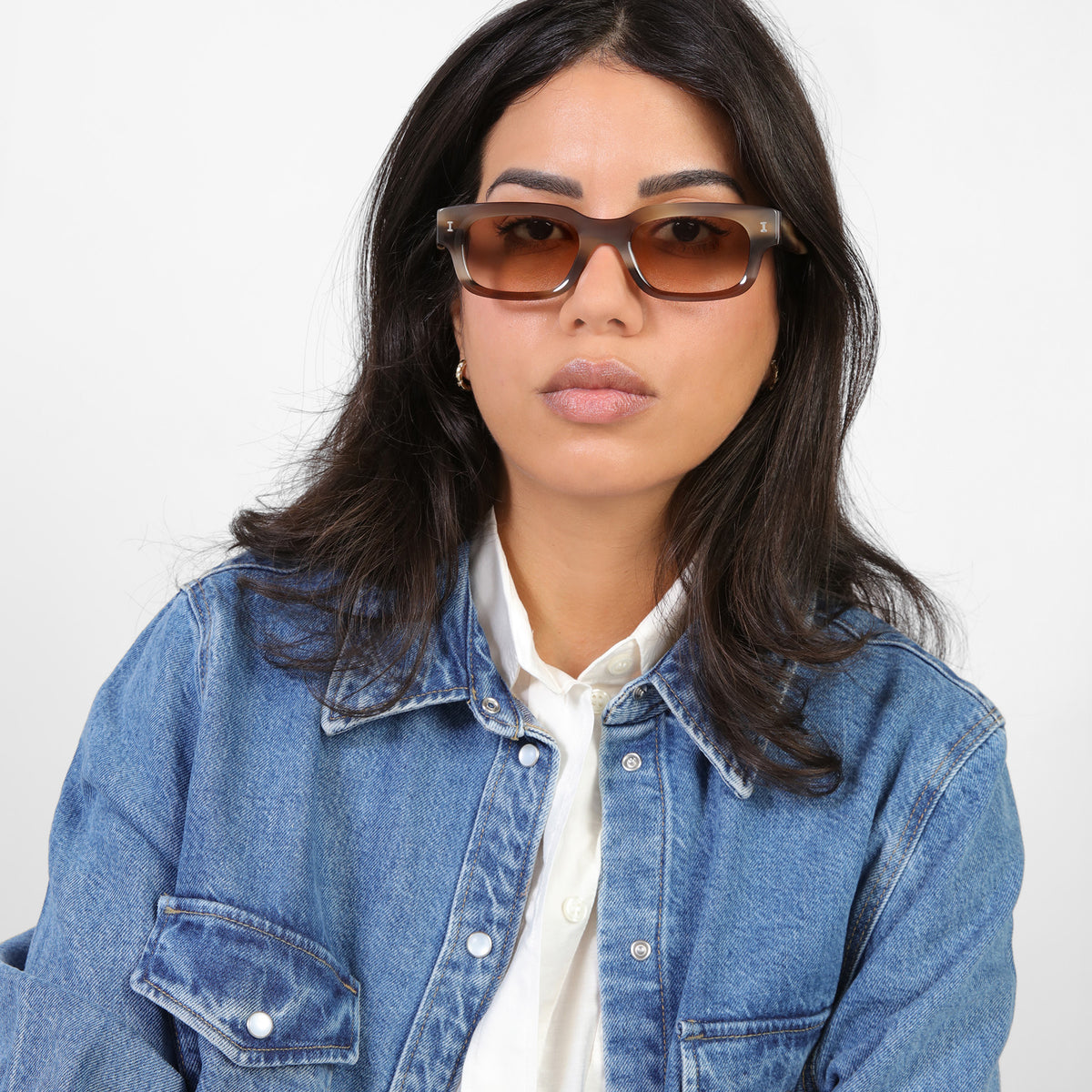 Woman wearing Cali E Sunglasses in Java with Taupe Gradient lenses, Brunette model in a denim jacket