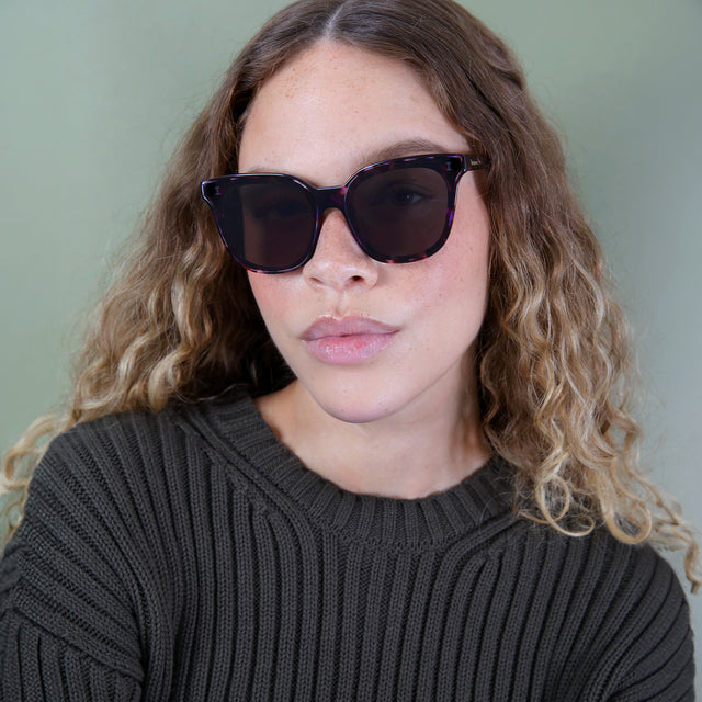 Brunette model with ombré, natural curls wearing Camille 64 Sunglasses Berry Tortoise with Grey Flat
