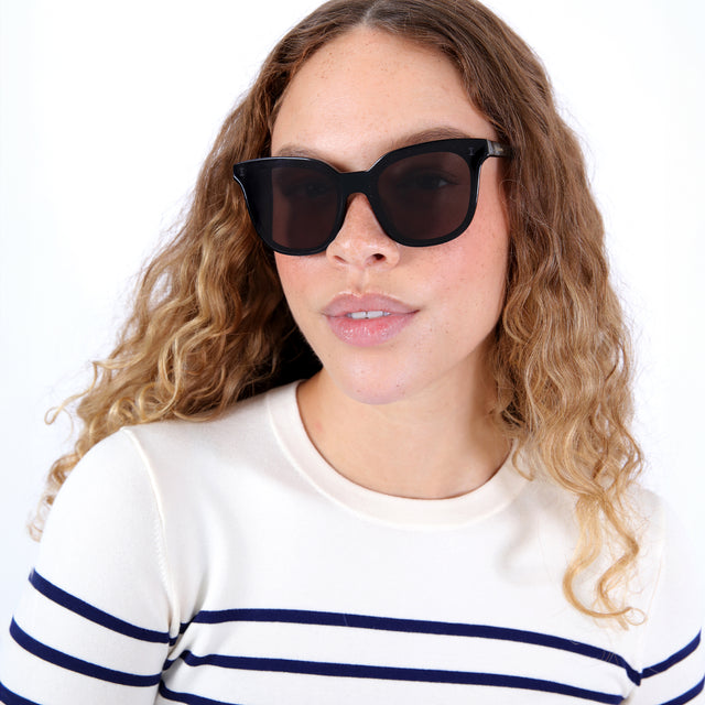 Brunette model with ombré, natural curls wearing Camille 64 Sunglasses Black with Grey Flat