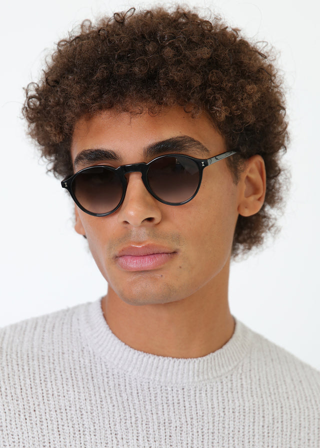 Man with curly brown hair wearing Capri Sunglasses Black with Olive Gradient