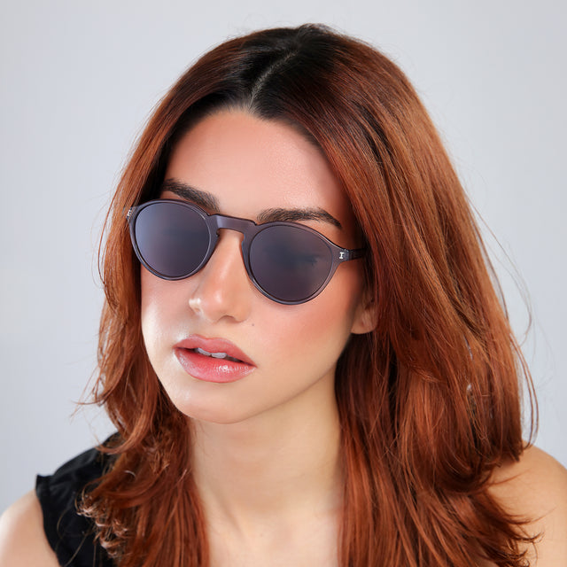 Woman with red hair in a black blouse looking down wearing Capri Sunglasses Mercury with Grey