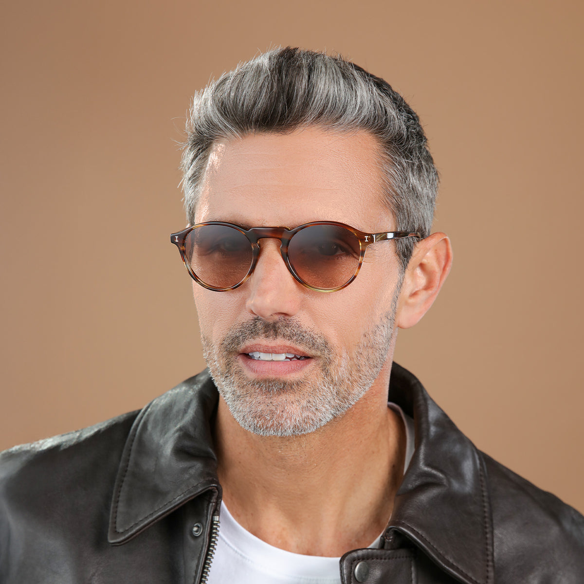 Man wearing Capri Sunglasses in Sand Dune with Brown Gradient lenses, front view, Man in a black leather jacket glancing left