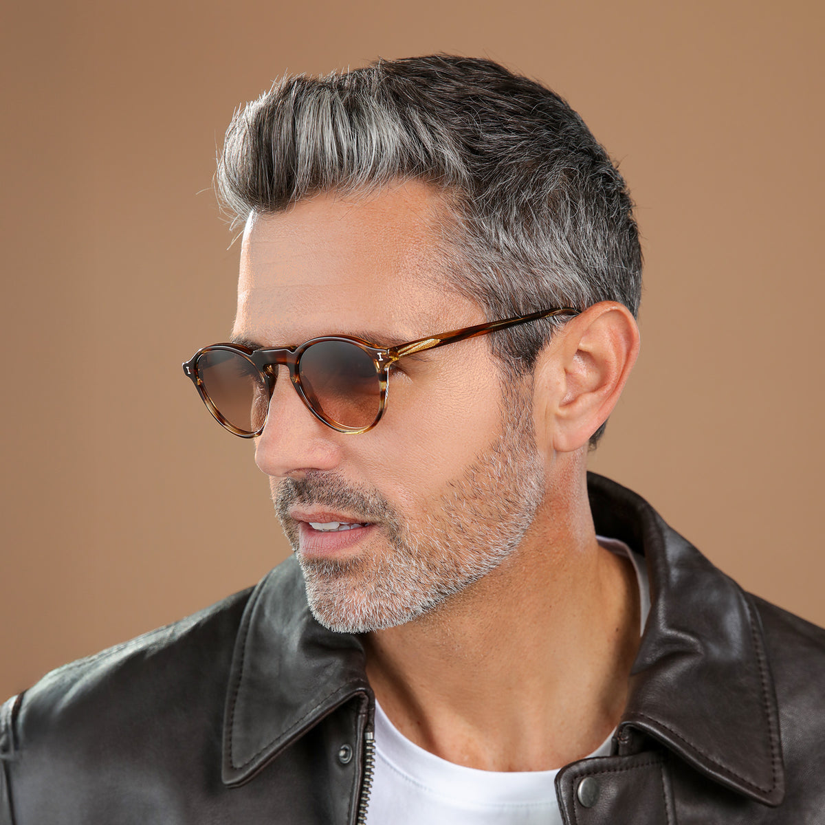 Man wearing Capri Sunglasses in Sand Dune with Brown Gradient lenses, side profile, Model with salt and pepper hair and beard in a black leather jacket looking right