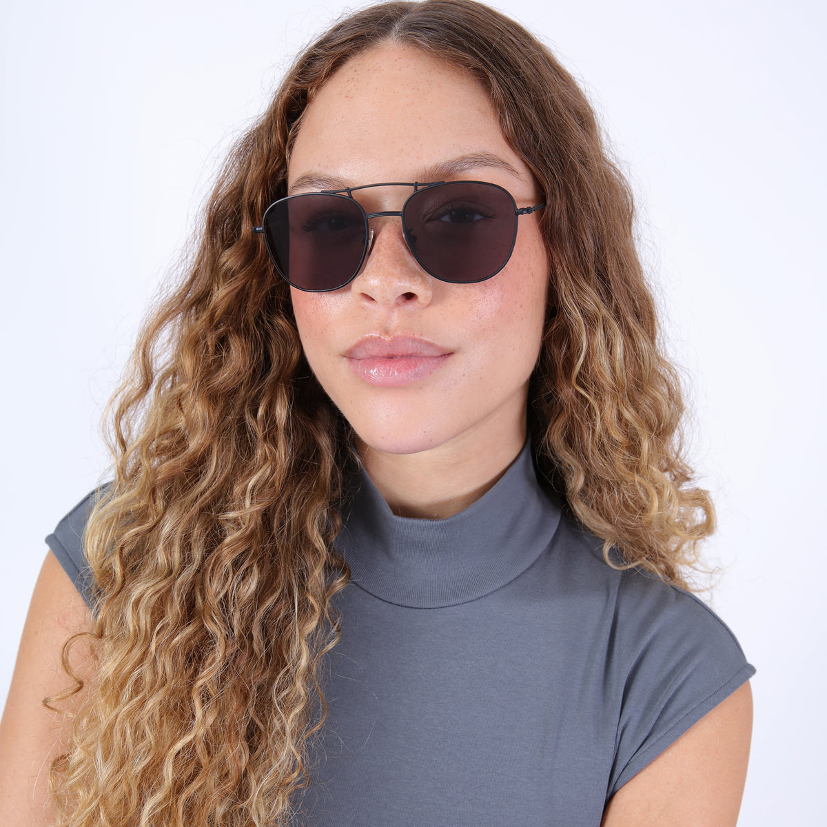 Woman wearing Cyprus Sunglasses in Matte Black with Grey Flat lenses, Brunette model with ombré, natural curls