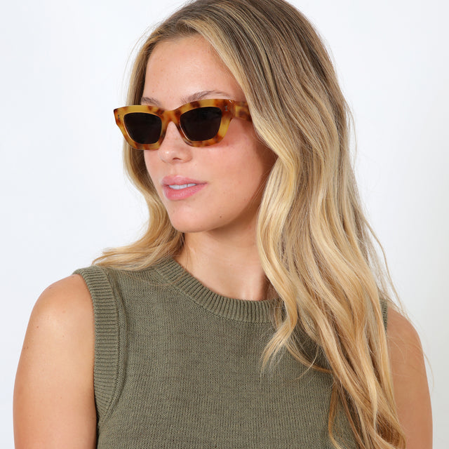 Blonde model with loose curls wearing Donna Sunglasses Amber with Grey
