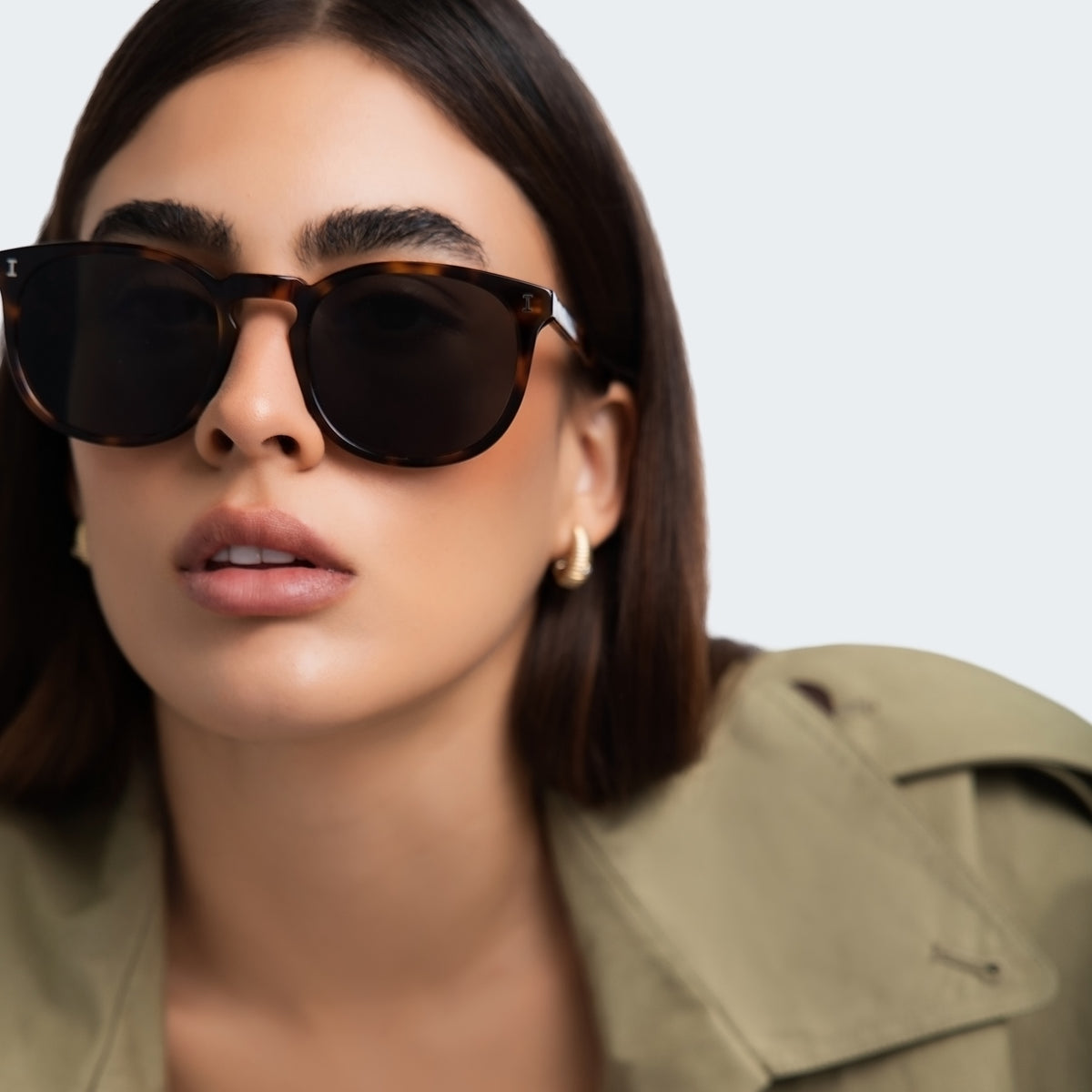 Woman wearing Eldridge 56 Sunglasses in Havana with Dark Olive Flat lenses, front view, Woman in a trench coat
