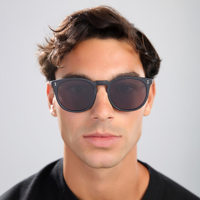 Man with brown hair in a black tee wearing Eldridge 56 Sunglasses Matte Black with Grey Flat