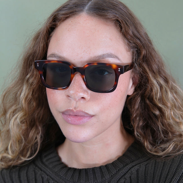 Brunette model with ombre, wavy hair wearing Ellison Sunglasses Havana with Olive Flat