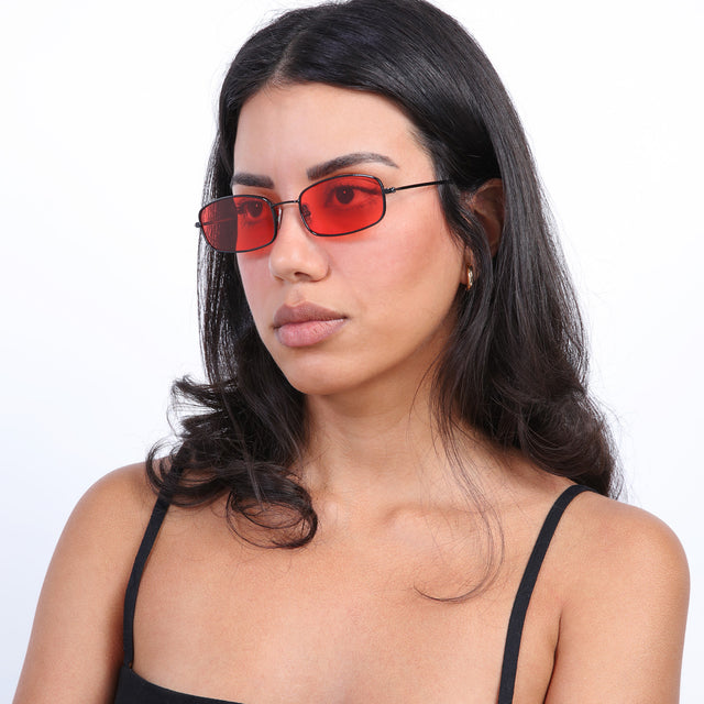 Brunette model with loose curls looking right wearing Flushing Sunglasses Black with Red Flat See Through