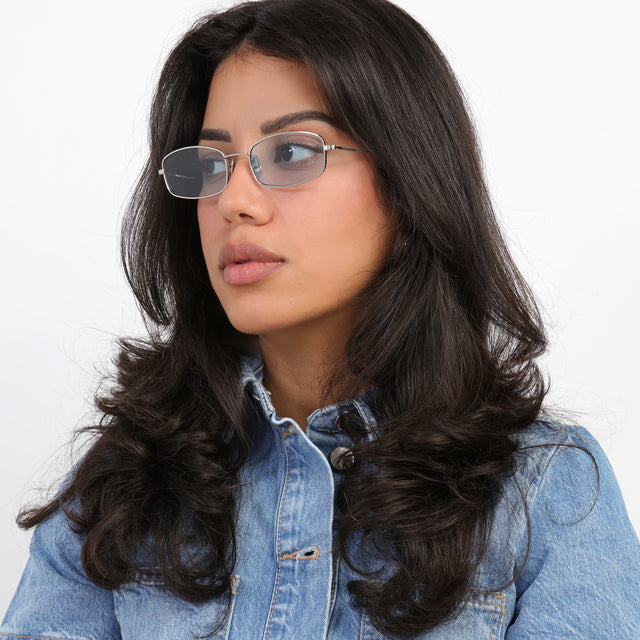 Brunette model with loose curls looking right wearing Flushing Sunglasses Silver with Light Blue Flat See Through
