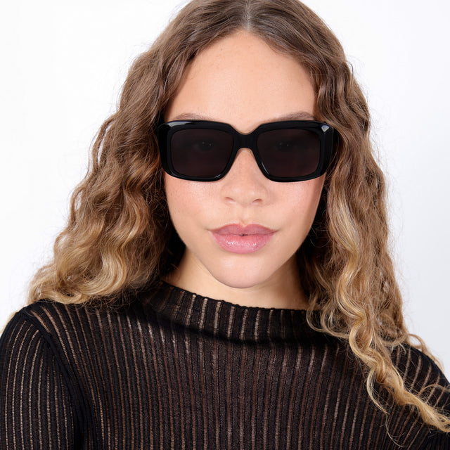 Brunette model with ombré, natural curls wearing Geno Sunglasses Black with Grey