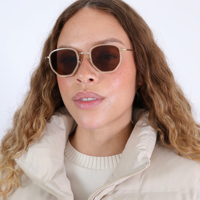Brunette model with wavy hair in a white puffer coat wearing Hunter Ace Sunglasses Champagne/Gold with Brown