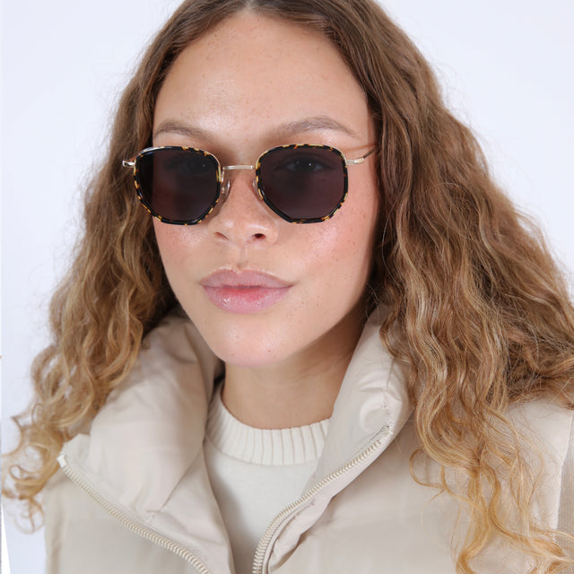 Brunette model with wavy hair in a white puffer coat wearing Hunter Ace Sunglasses Flame/Gold with Grey