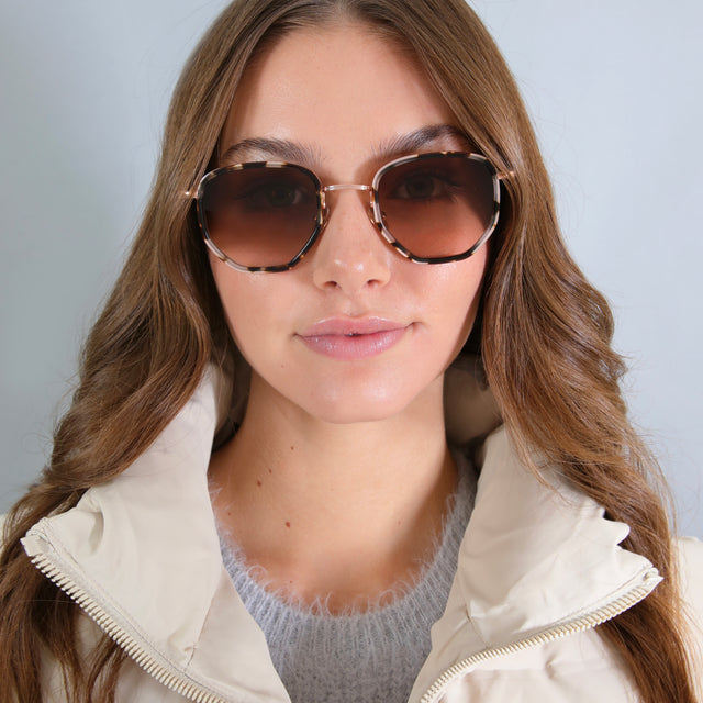 Brunette model with curled hair in a white puffer coat wearing Hunter Ace Sunglasses White Tortoise/Rose Gold with Brown Gradient
