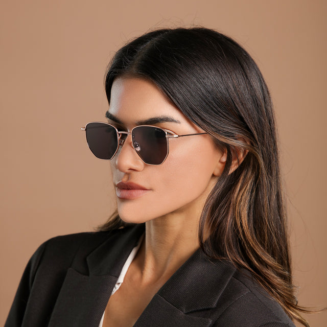Angled view of brunette model in a black blazer wearing Hunter Sunglasses Rose Gold with Grey