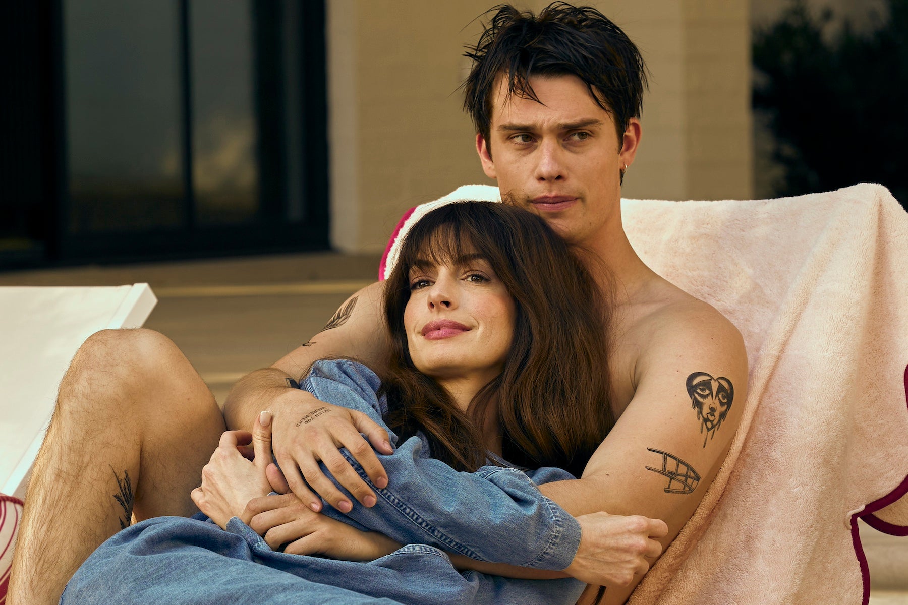 Still from 'The Idea of You' featuring Anne Hathaway and Nicholas Galitzine embracing each other on a tanning chair
